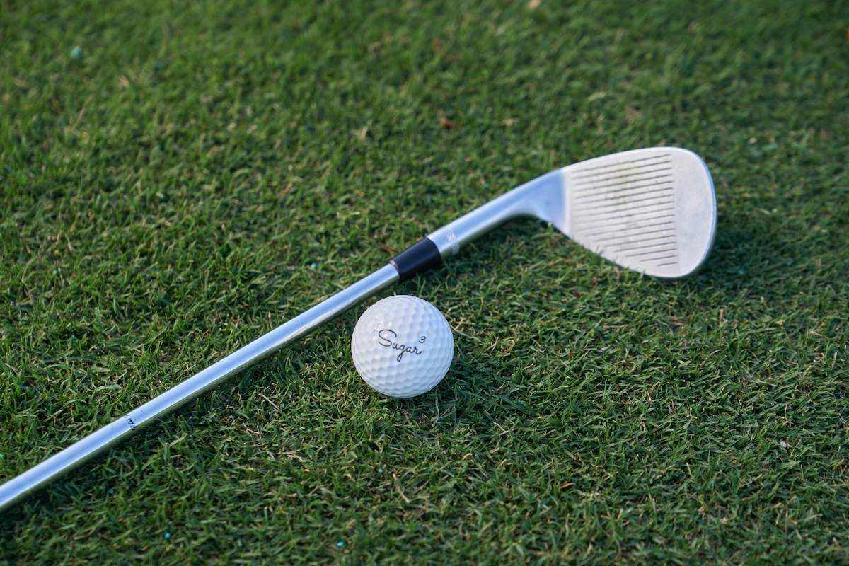 An iron lying on the grass next to a golf ball