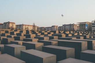 A vast array of gray concrete slabs arranged in a grid pattern, set against a backdrop of residential buildings. In the sky, a balloon can be seen in the distance, with a clear backdrop of a blue sky.