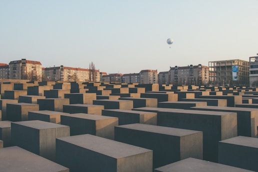 A vast array of gray concrete slabs arranged in a grid pattern, set against a backdrop of residential buildings. In the sky, a balloon can be seen in the distance, with a clear backdrop of a blue sky.