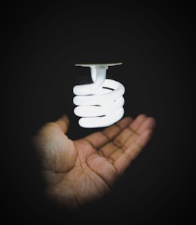 Close-up of hands unscrewing an old light bulb from a modern lamp.