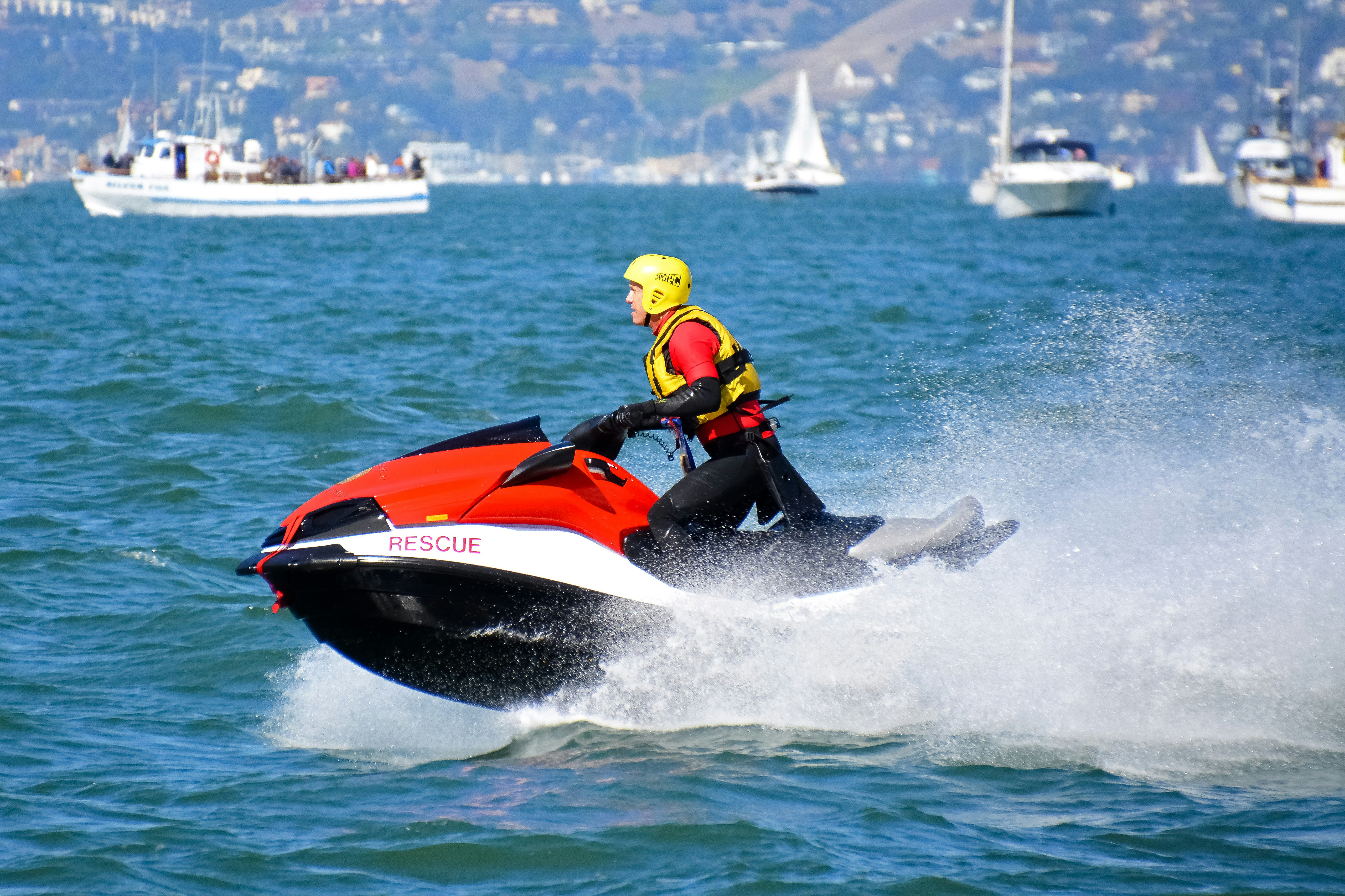 man in yellow and black suit riding red and white personal watercraft during daytime