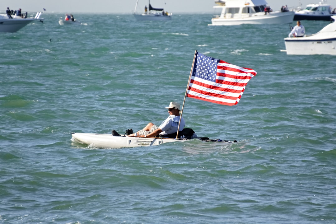 man in black shirt riding on white kayak holding us a flag during daytime