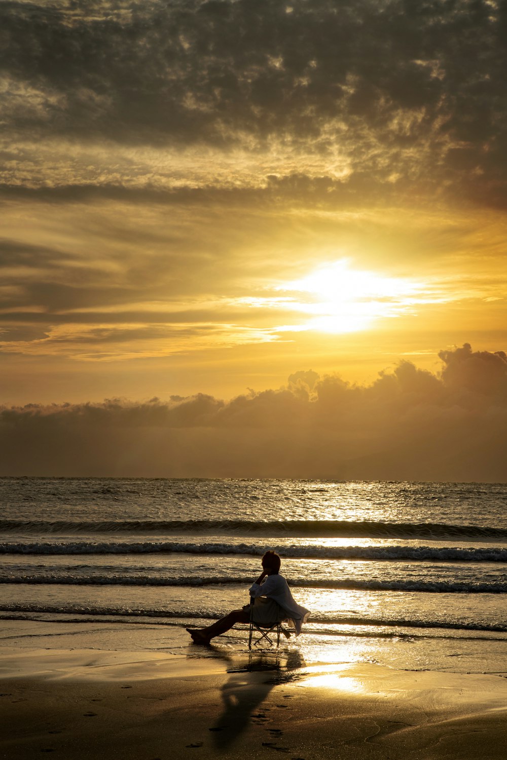 woman in white shirt sitting on beach during sunset