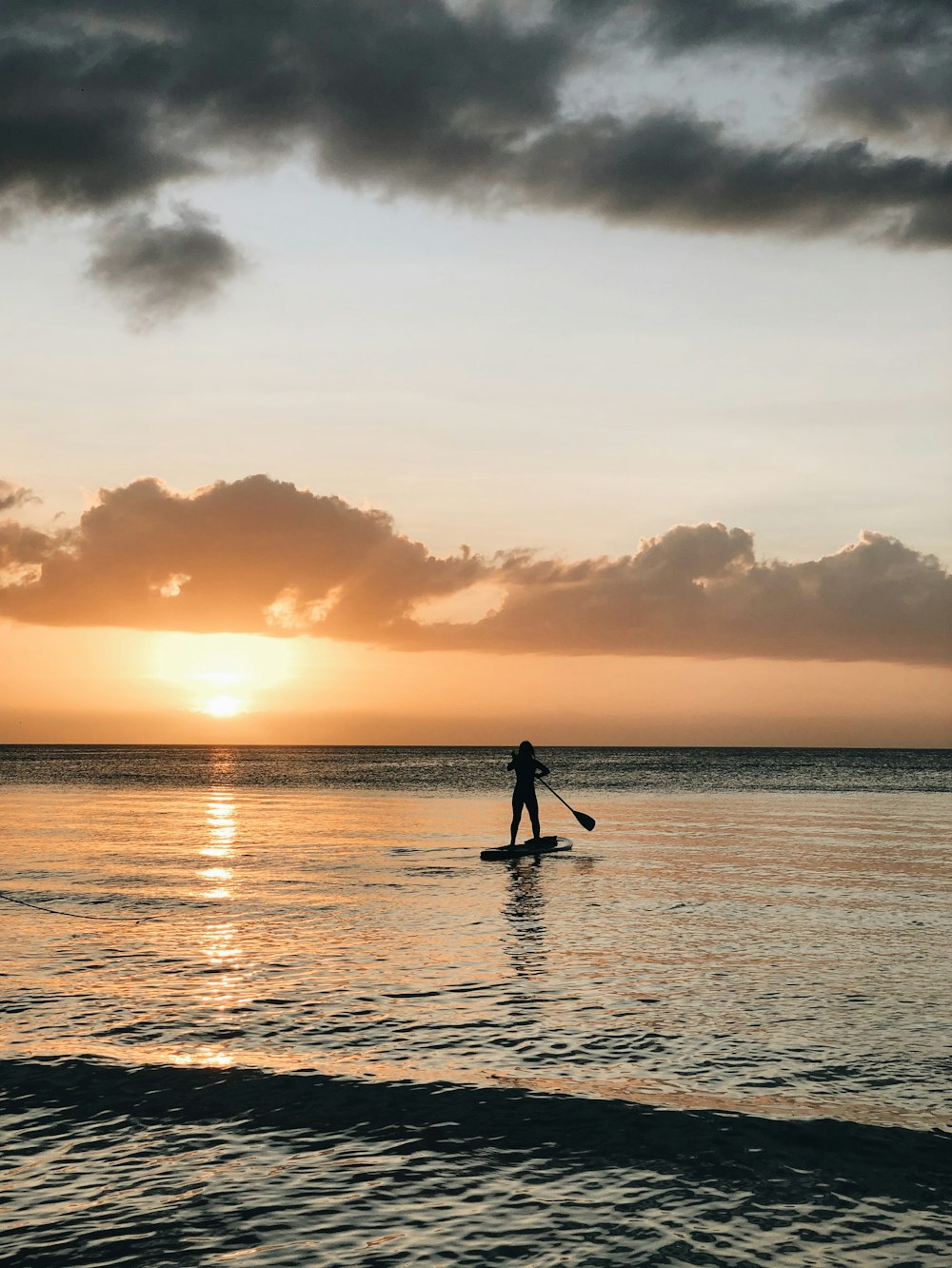 silhouette of person standing on sea shore during sunset