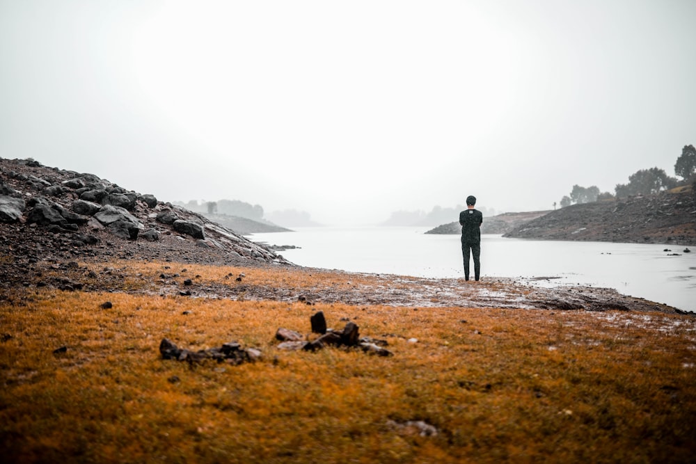 Persona in piedi sul campo marrone vicino allo specchio d'acqua durante il giorno