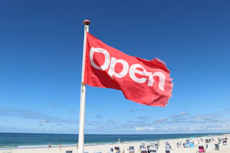 a red open flag on a beach next to the ocean