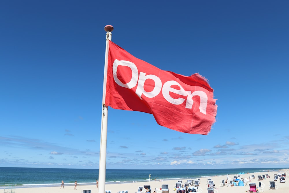 a red open flag on a beach next to the ocean