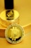 A stack of shiny, gold-like cryptocurrency coins featuring the logos of Ethereum and Bitcoin. The coins have a metallic sheen, with the Ethereum coin displaying a triangular symbol and Bitcoin displaying a 'B' with two vertical lines running through it.