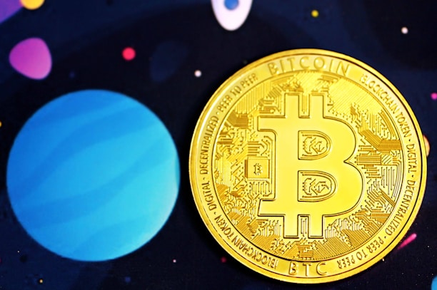 A golden Bitcoin coin adorned with intricate circuit designs is prominently placed against a background that is reminiscent of outer space, featuring large planet-like shapes in shades of blue and purple and small scattered dots in various colors.