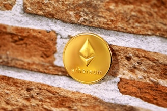 A shiny gold Ethereum coin is positioned against a textured brick wall, featuring the Ethereum logo prominently in the center.