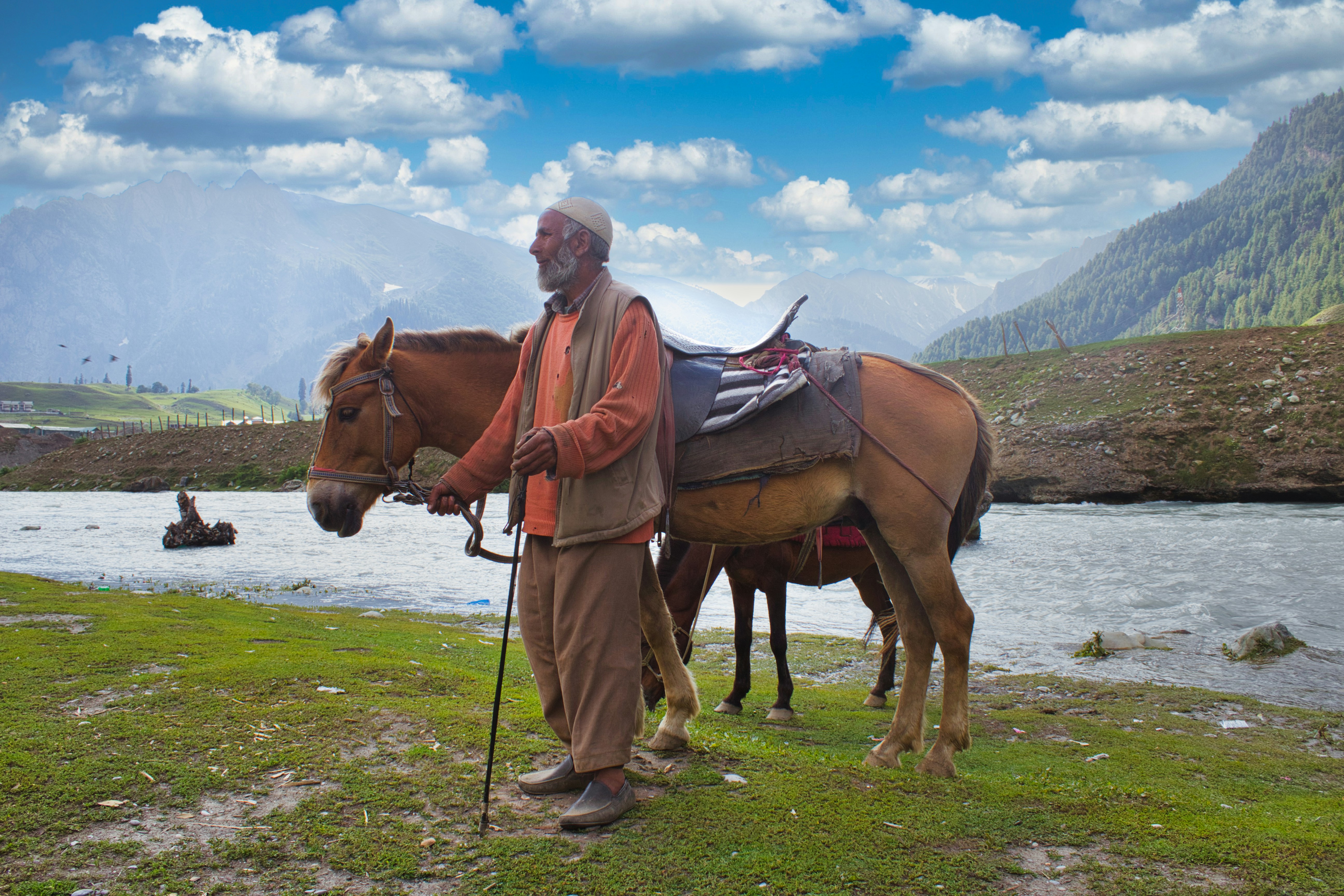 man in white long sleeve shirt and brown pants standing beside brown horse during daytime