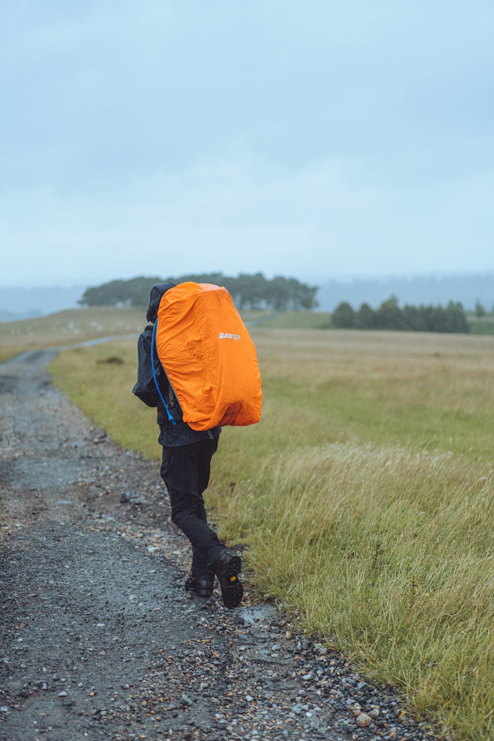 person in orange and black jacket walking on dirt road during daytime