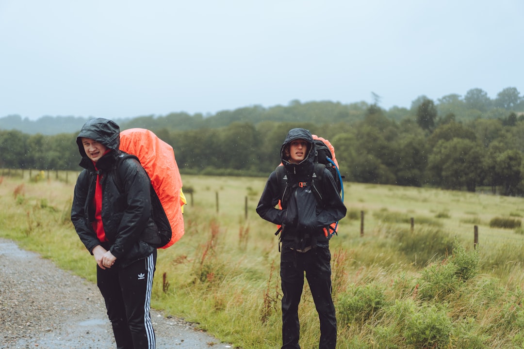 man in black and red jacket and black pants standing on gray dirt road during daytime