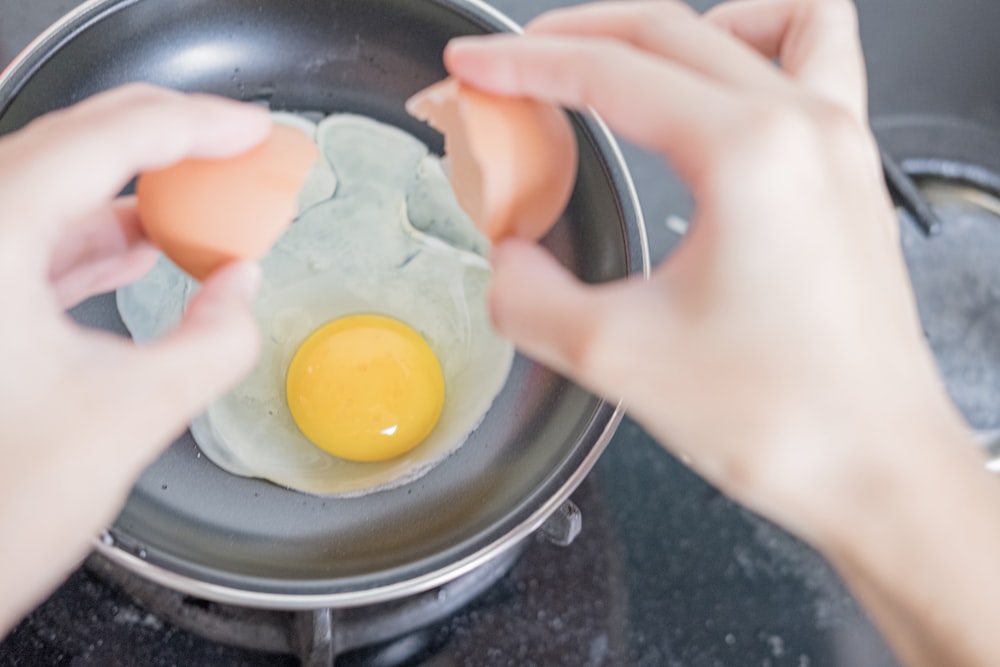person holding black frying pan with egg