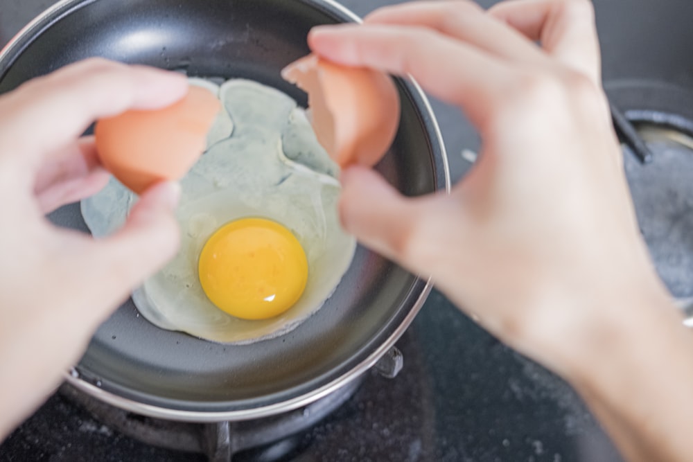 person holding black frying pan with egg