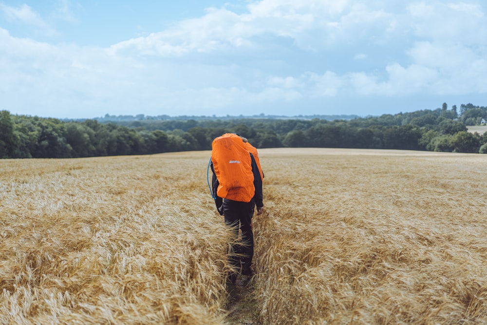 person in orange jacket standing on brown grass field during daytime