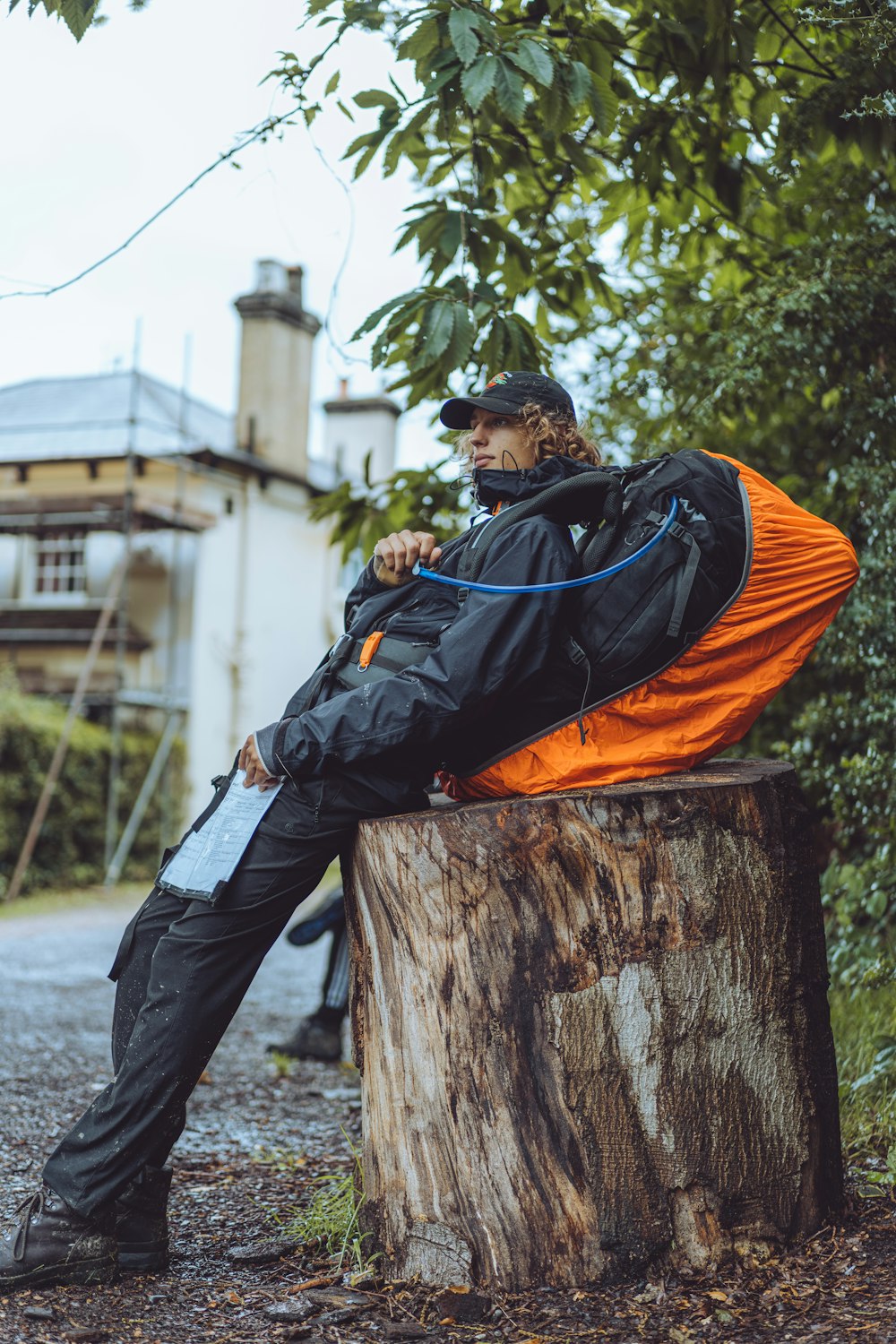 man in orange and black jacket and blue denim jeans sitting on brown wooden log during