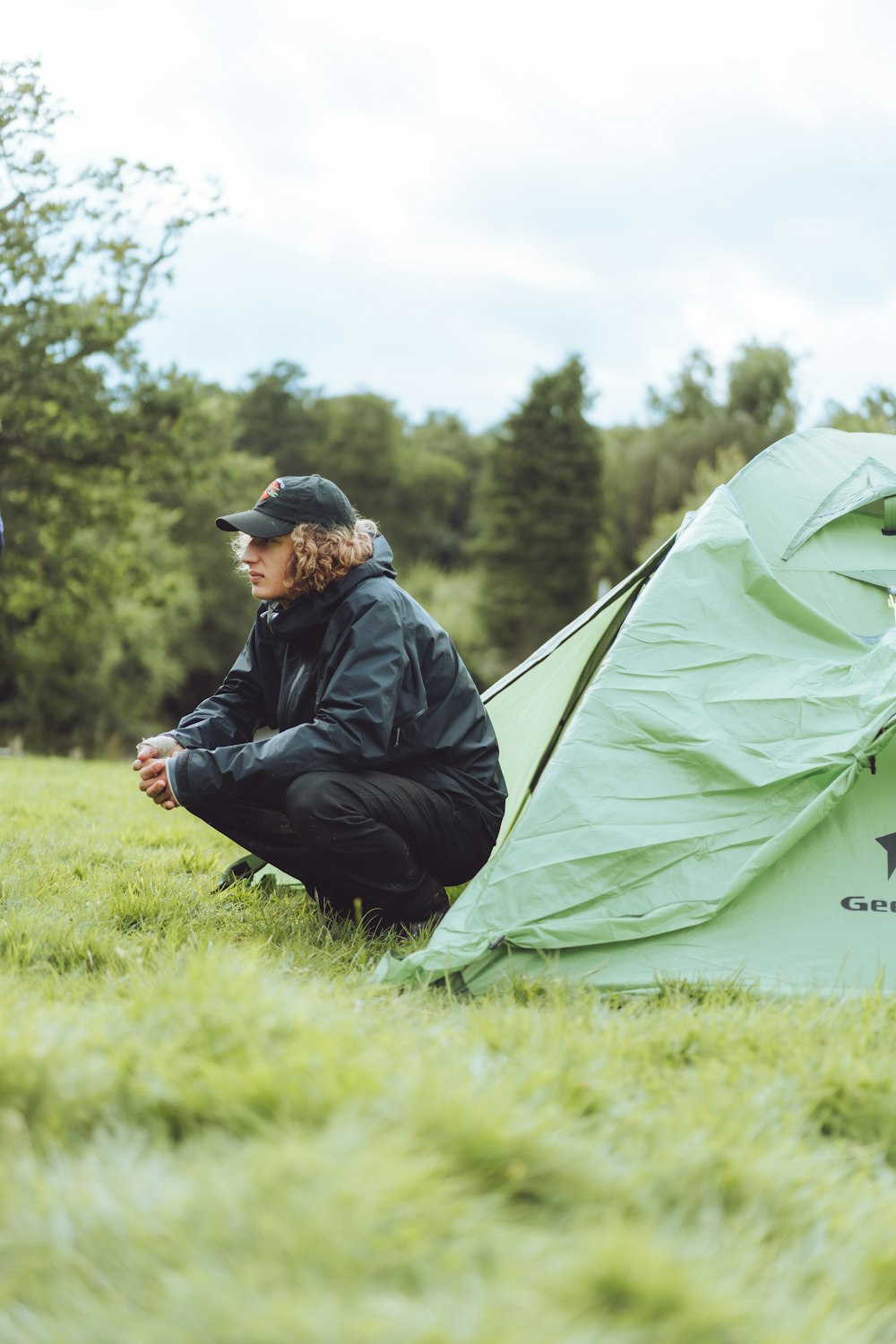 uomo in giacca nera che si siede sulla tenda verde durante il giorno