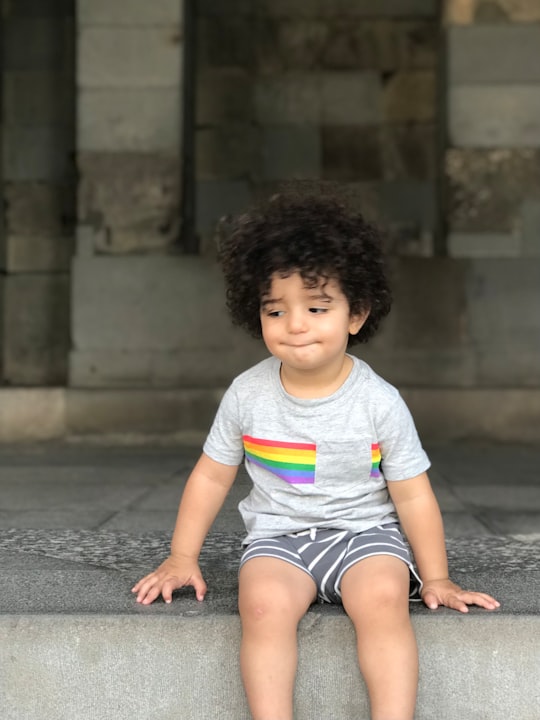 boy in white crew neck t-shirt and blue shorts sitting on gray concrete floor in Garni Armenia