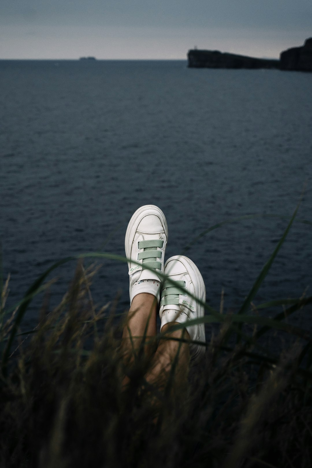 person wearing white sneakers standing on green grass near body of water during daytime