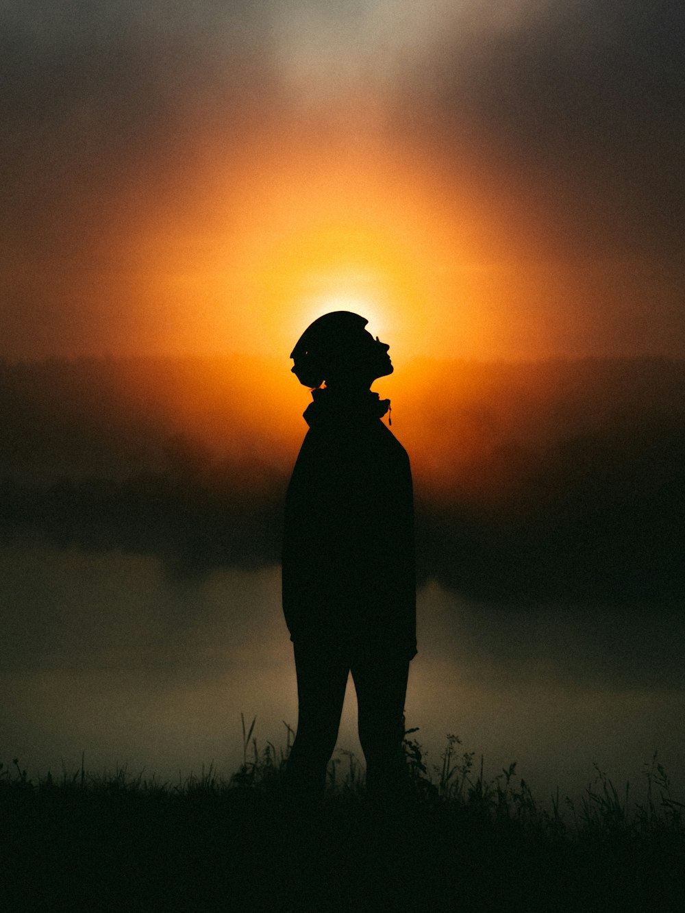 silhouette of man standing on grass field during sunset