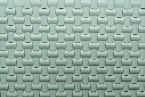 A repeating pattern of curved tiles creates a textured, three-dimensional surface. The tiles are arranged in an interlocking design with a smooth, glossy finish.