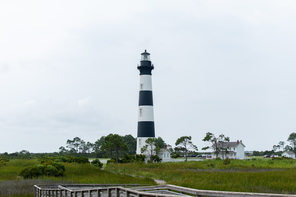 Phare blanc et noir près d’un champ d’herbe verte sous un ciel blanc pendant la journée