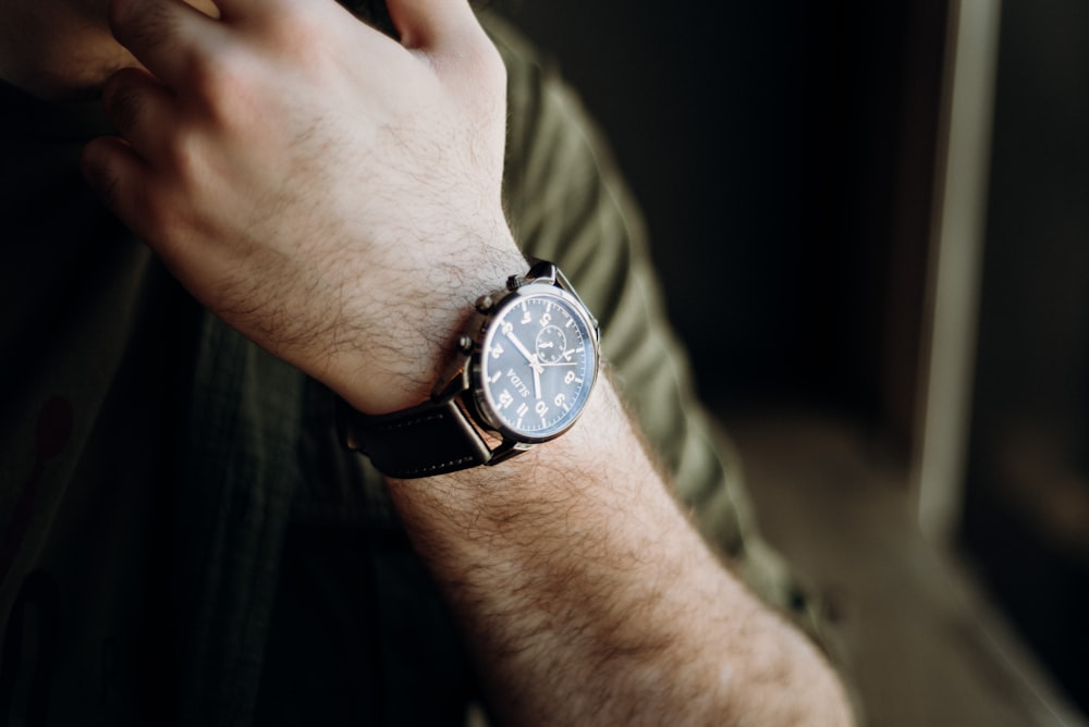 person wearing black leather strap silver round analog watch