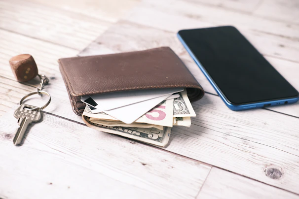 Close-up of a stylish leather wallet and minimalist keys placed beside a modern smartphone on a marble countertop.