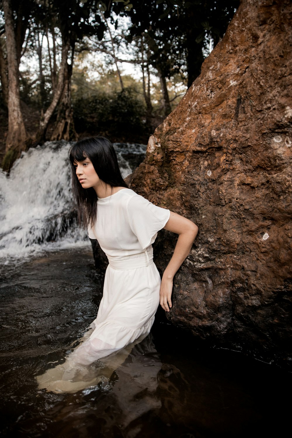 woman in white dress standing beside brown rock