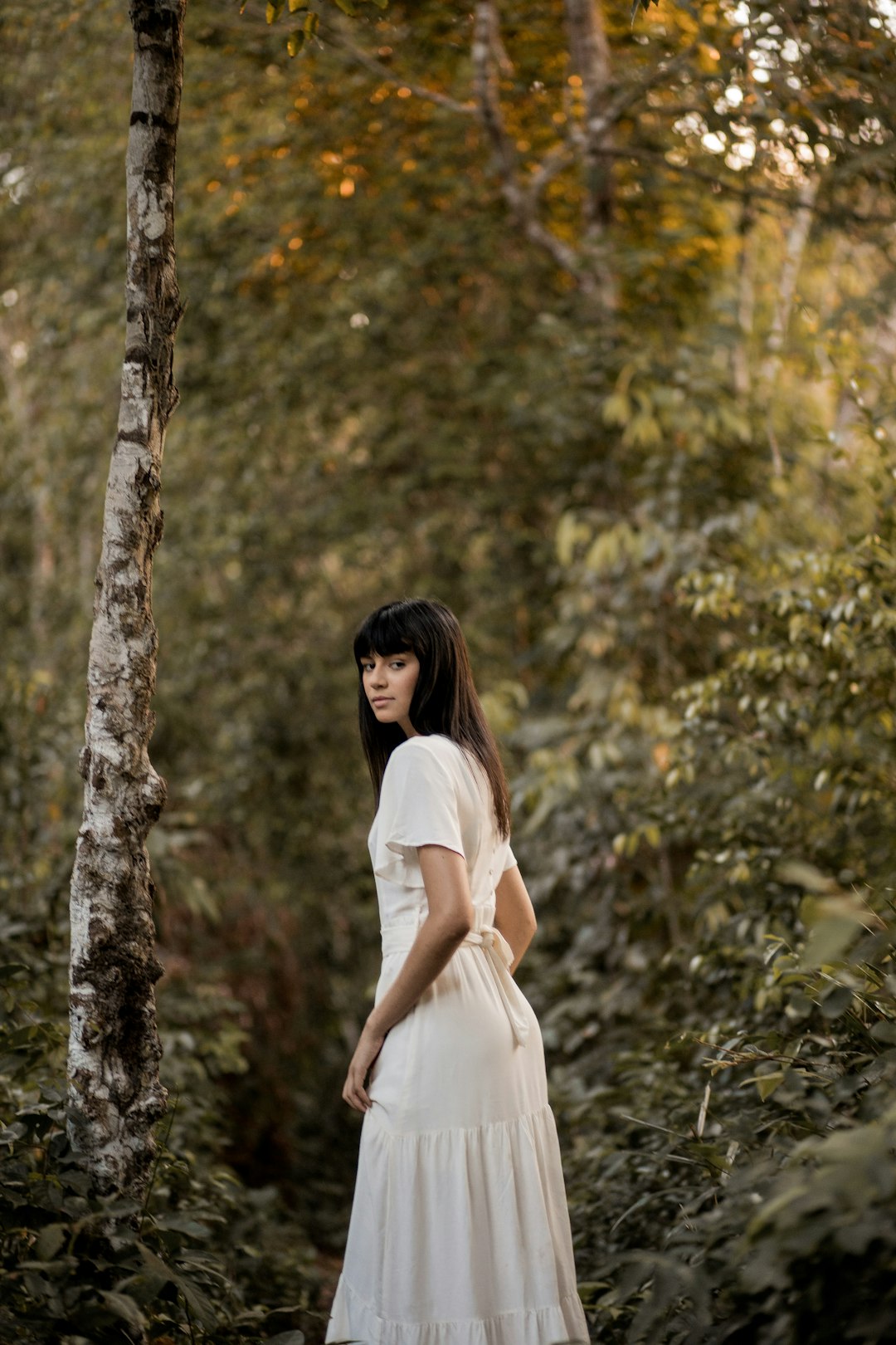 woman in white dress standing beside tree during daytime