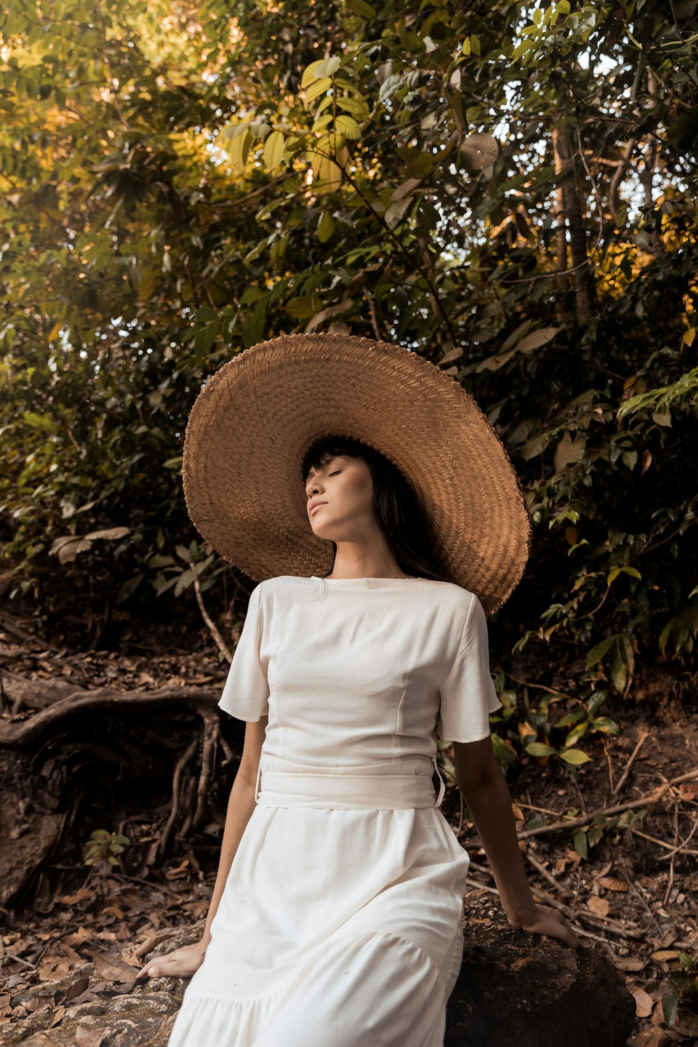 woman in white dress wearing brown straw hat standing near green plants
