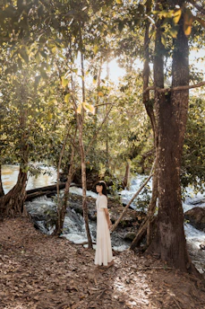 A serene woman sitting cross-legged in a sunlit forest clearing, surrounded by soft greenery and gentle rays of light.