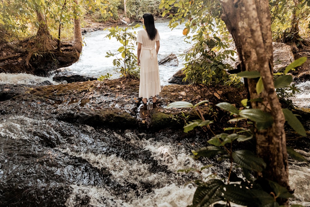 woman in white dress standing on rocky river during daytime