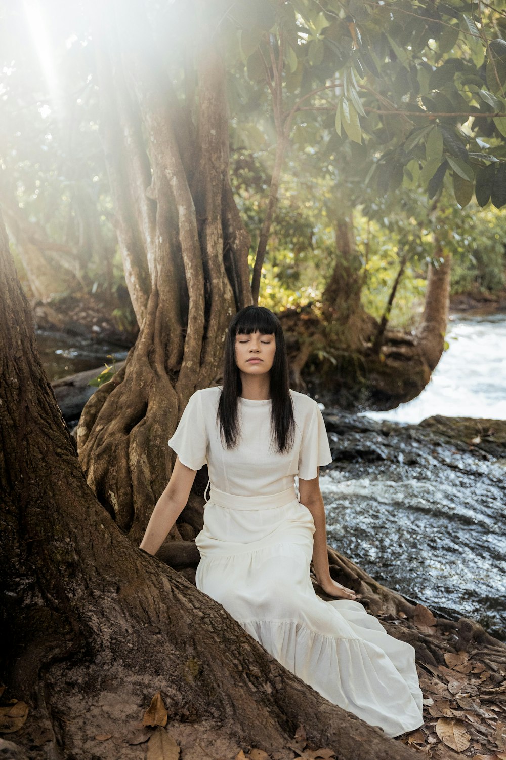 woman in white dress sitting on brown tree trunk