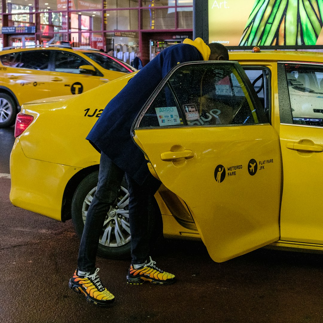 person in black pants and black boots standing beside yellow taxi cab