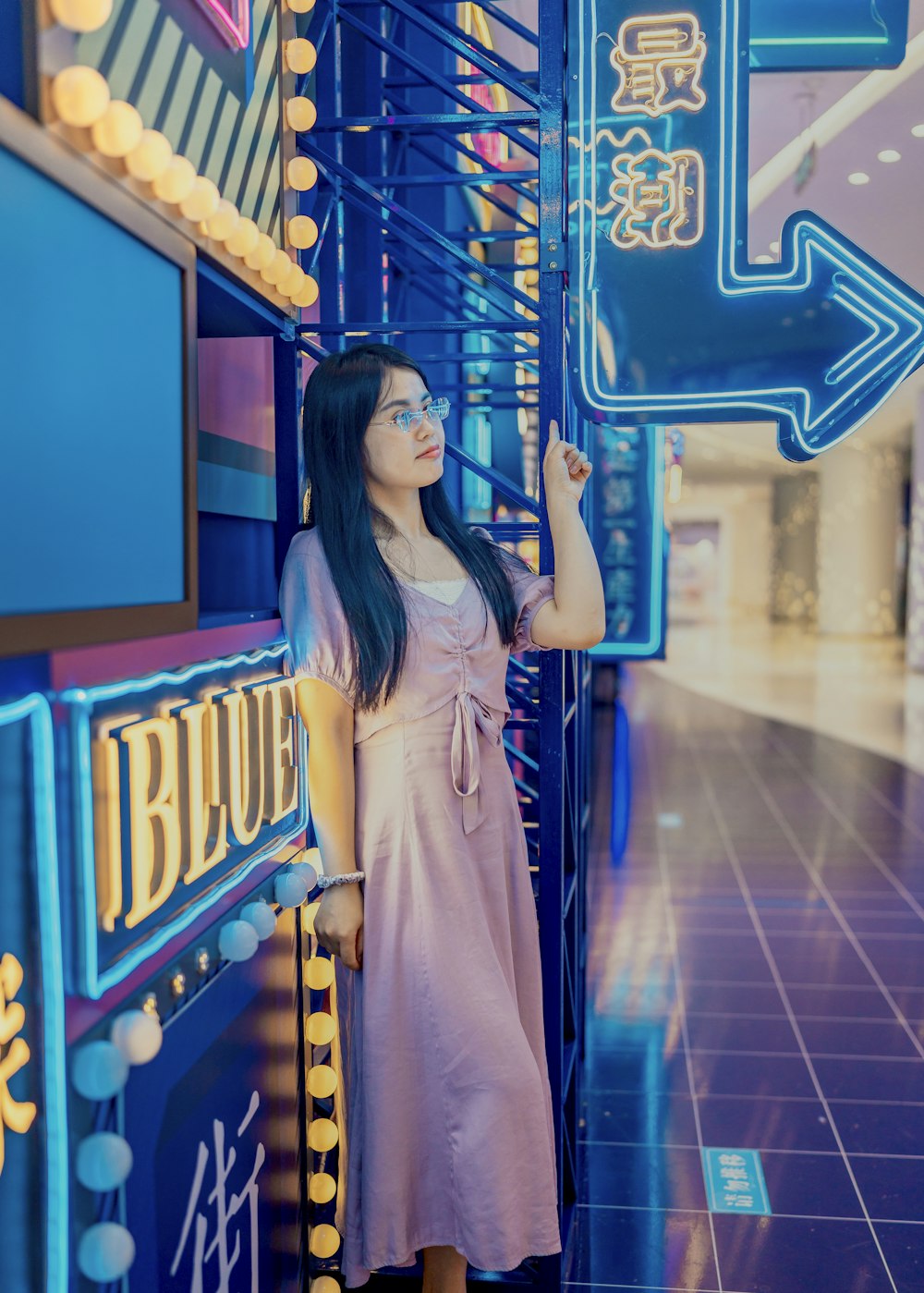 woman in white dress standing near blue and yellow neon sign