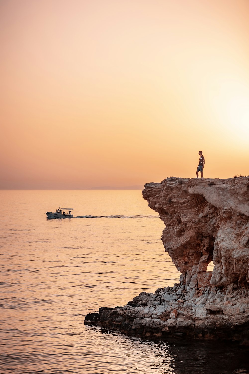 silhouette of person standing on rock formation near body of water during sunset