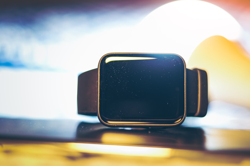 Close-up of a sleek smart watch glowing with blue light on a black background.