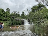 A group of friends enjoying a clear blue natural pool surrounded by rocks and greenery.