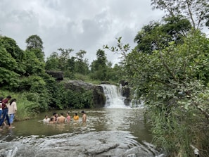 A group of friends enjoying a clear blue natural pool surrounded by rocks and greenery.