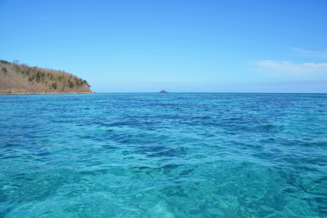 blue sea near brown and green mountain under blue sky during daytime