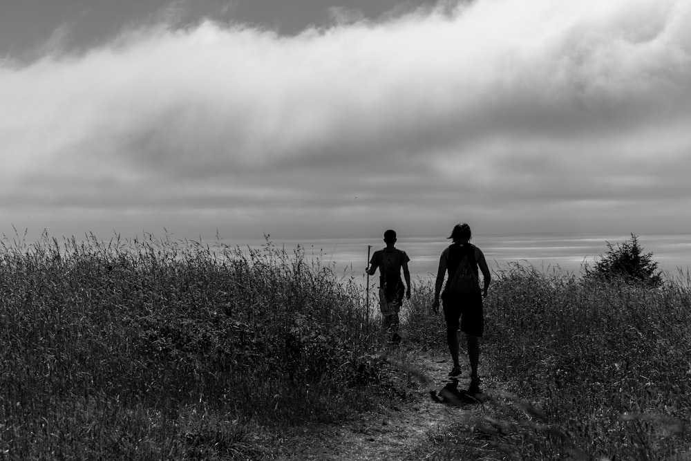 man and woman walking on grass field in grayscale photography
