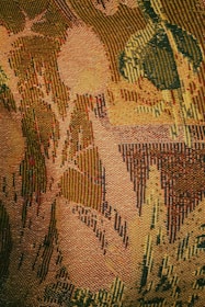 An intricately woven tapestry showcasing an abstract pattern with various shapes that resemble leaves and foliage. The texture is rich and detailed, with visible individual threads creating a sense of depth and complexity.