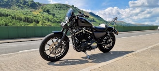 A scenic view of a winding road through lush green hills with a motorcycle parked nearby.