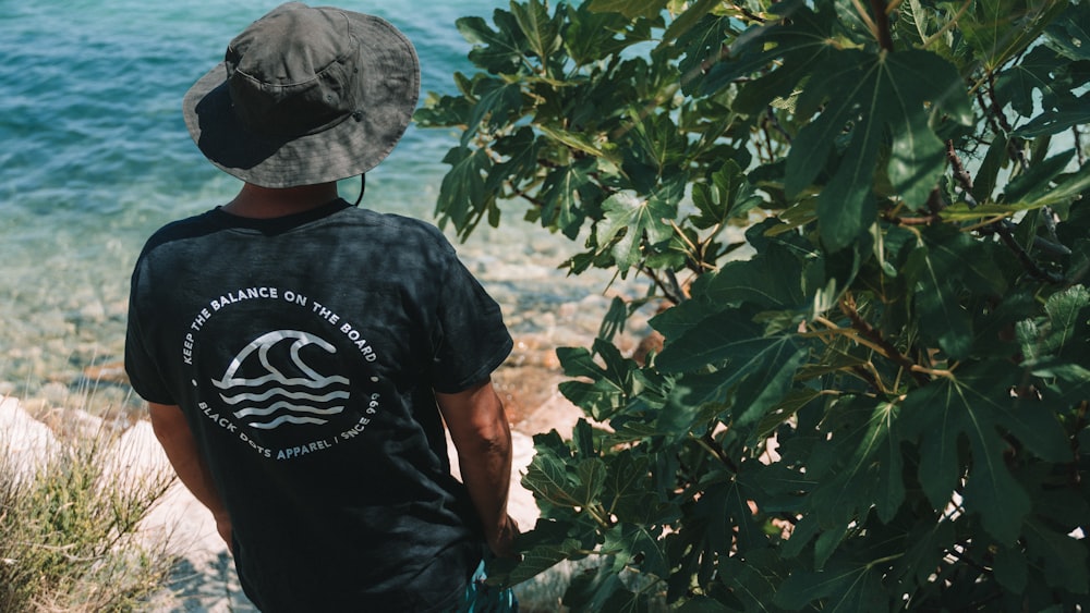 man in black crew neck t-shirt and gray cap standing near green plant during daytime