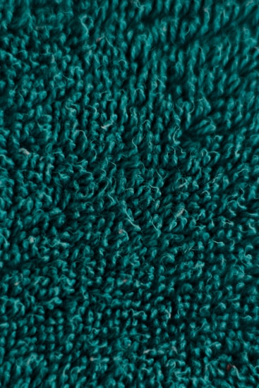 A close-up view of textured fabric with a fluffy, curly surface. The material appears soft and thick, with uniform depth and intricate looping patterns.