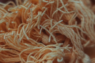 A close-up view of tangled yarn strands, primarily in shades of orange and cream. The texture appears soft and fibrous, with some yarn pieces twisted together creating a chaotic but aesthetically pleasing pattern.