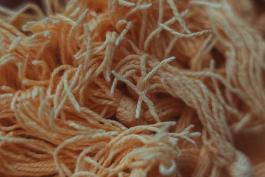 A close-up view of tangled yarn strands, primarily in shades of orange and cream. The texture appears soft and fibrous, with some yarn pieces twisted together creating a chaotic but aesthetically pleasing pattern.