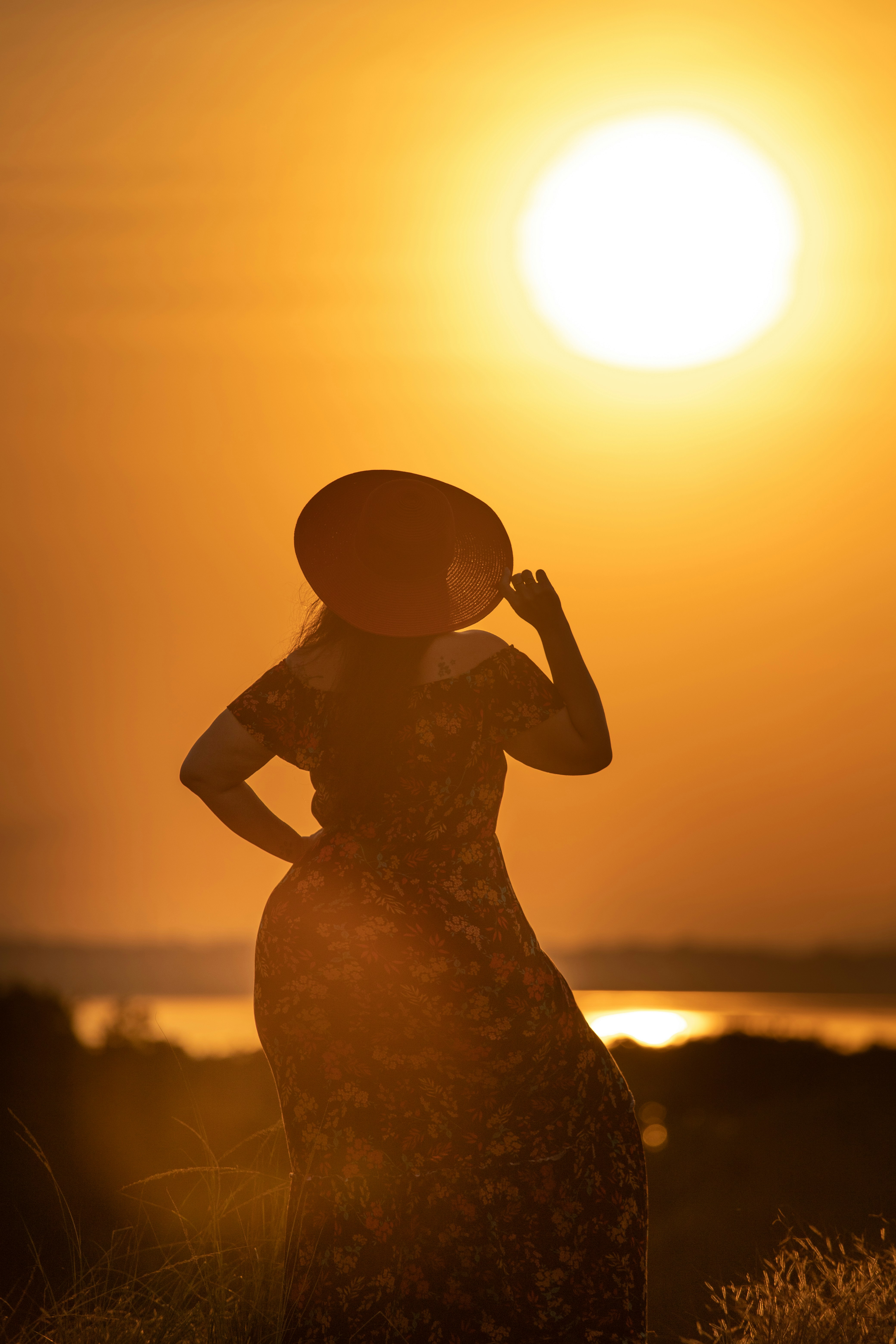 Person in a patterned dress standing in tall grass at sunset.